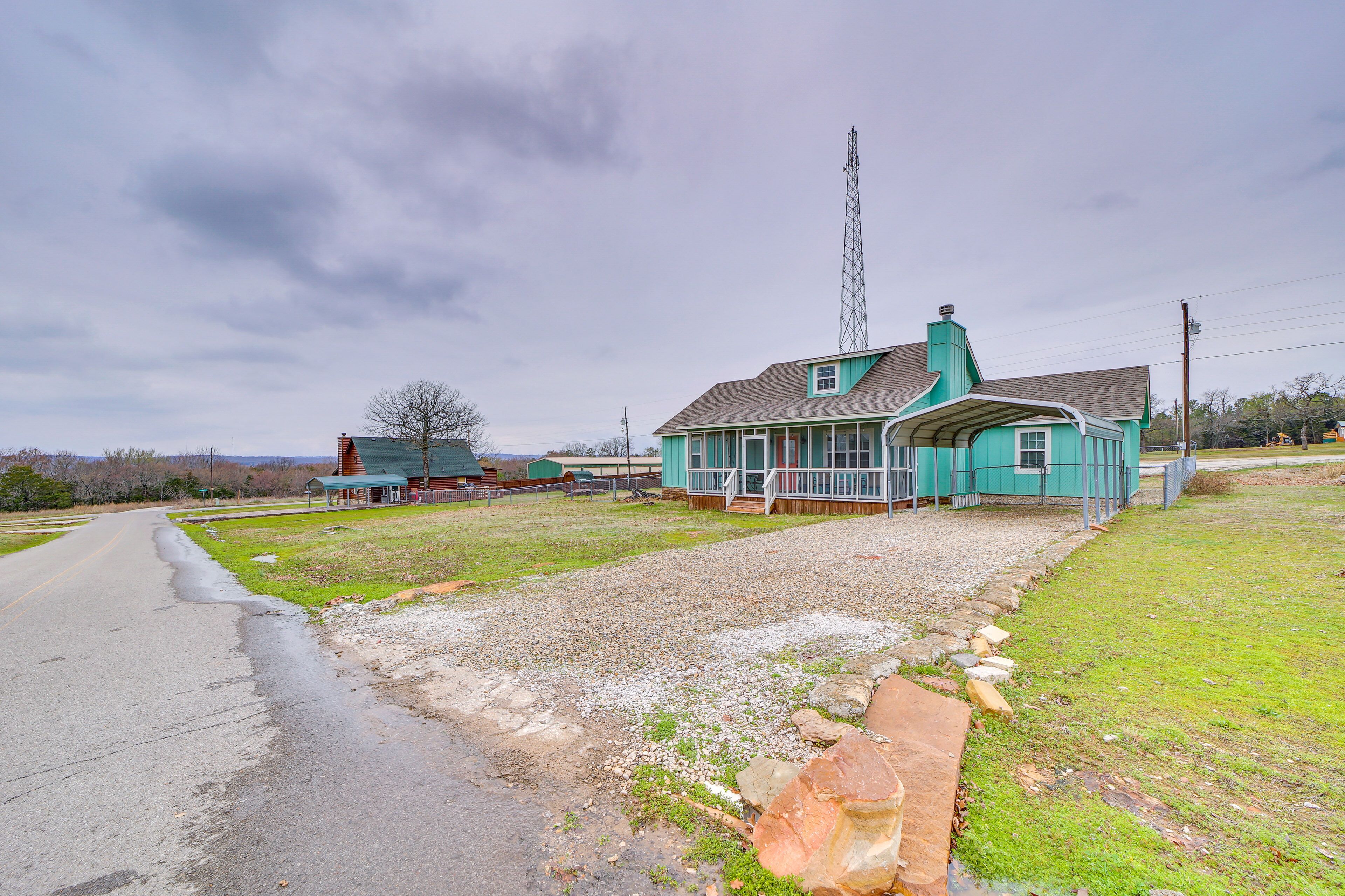 A house with a porch, a gravel driveway, and a tall communication tower in the background.