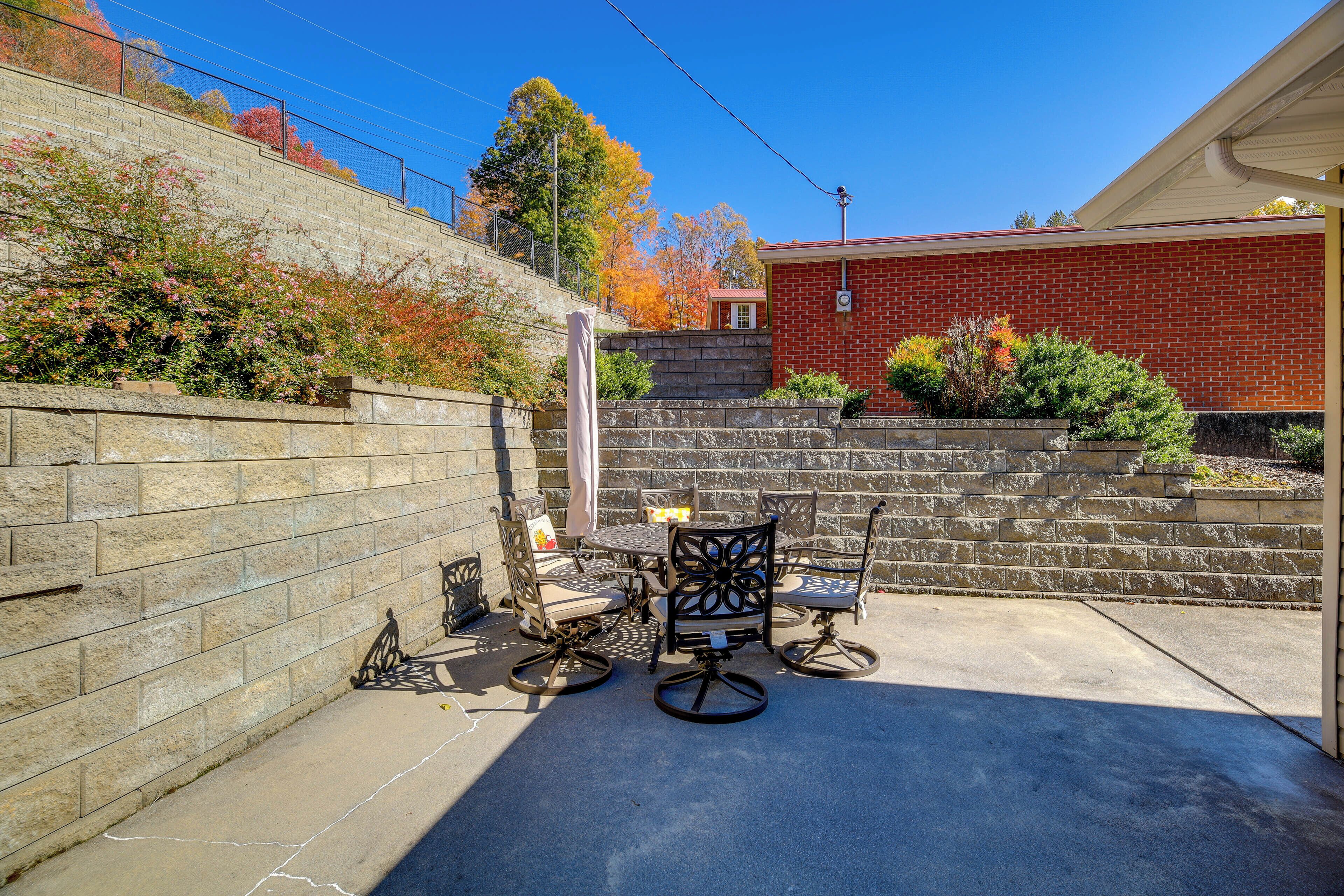 A patio area with a brick wall, a table with chairs, and a small garden with autumn foliage.