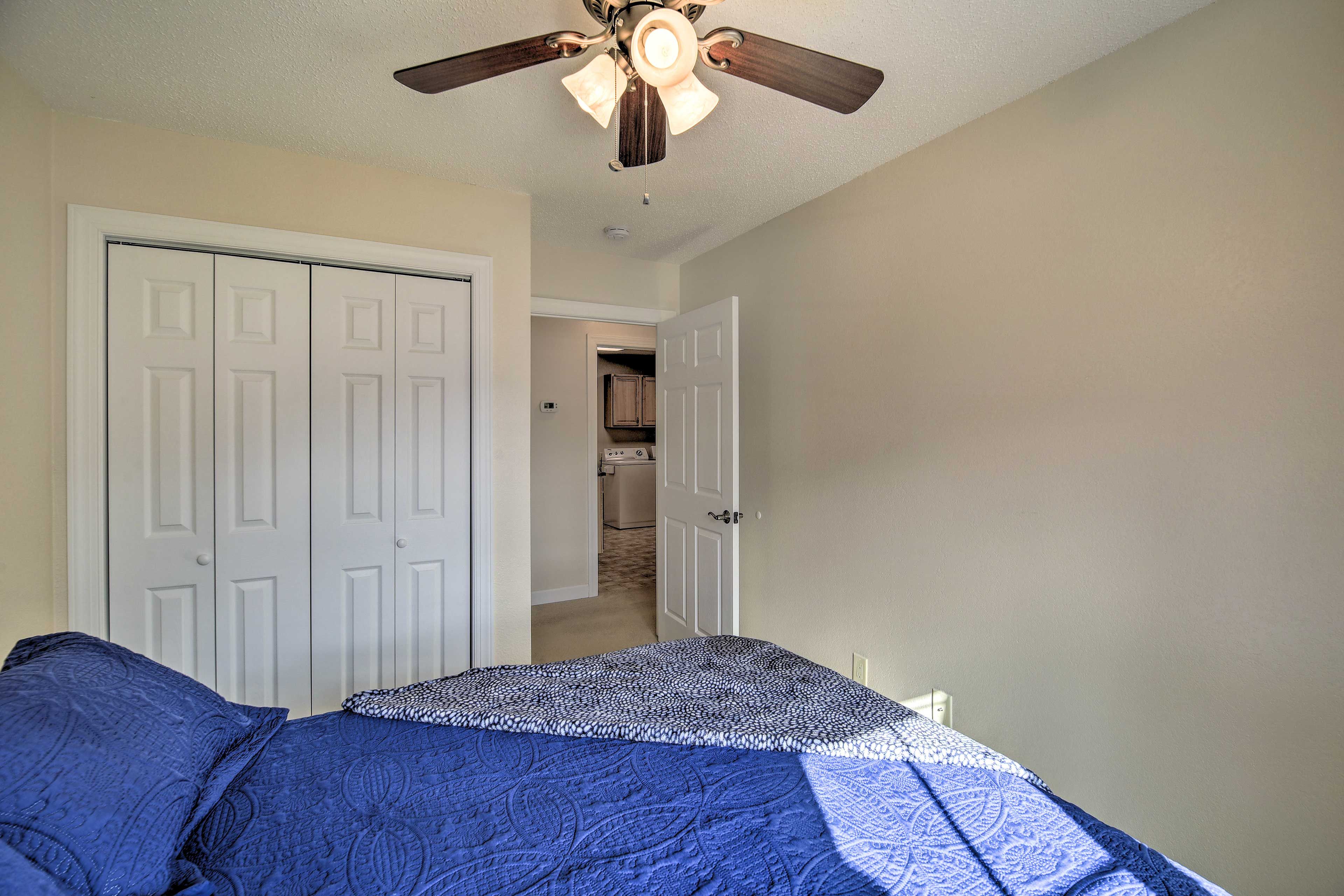 A bedroom with a bed, a ceiling fan, and a door leading to a hallway.