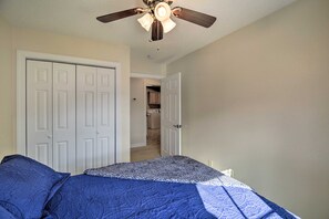 A bedroom with a bed, a ceiling fan, and a door leading to a hallway.