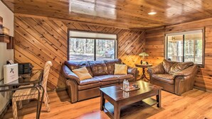 A cozy cabin interior with wooden walls, a leather sofa, a wooden coffee table, and a glass dining table.