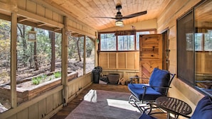 A wooden cabin with a covered porch, a ceiling fan, a large window, and a chair.