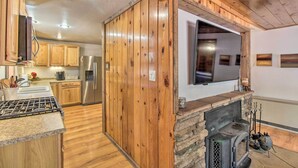 A modern kitchen with wooden cabinets, a stainless steel refrigerator, a built-in oven, and a stone fireplace.