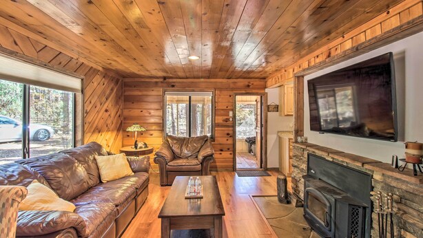 A cozy cabin interior with a leather sofa, a wooden coffee table, a fireplace, and a television mounted on the wall.