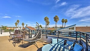 A rooftop patio with a swing chair, a cushioned seating area, and palm trees in the background.