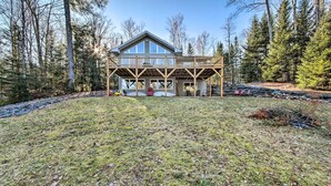 A two-story house with a wooden deck and a covered porch. - Stunning Monson Getaway on the Water! (Monson)