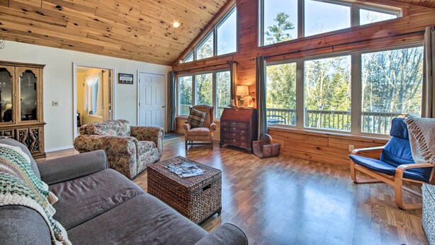 A spacious living room with wooden floors, large windows, and a cozy fireplace. - Stunning Monson Getaway on the Water! (Monson)