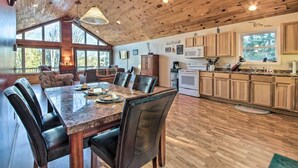 A spacious dining area with a wooden ceiling, large windows, and a kitchen with wooden cabinets and a microwave. - Stunning Monson Getaway on the Water! (Monson)