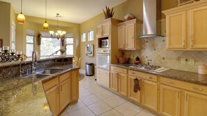 A kitchen with granite countertops, wooden cabinets, stainless steel appliances, and pendant lighting.
