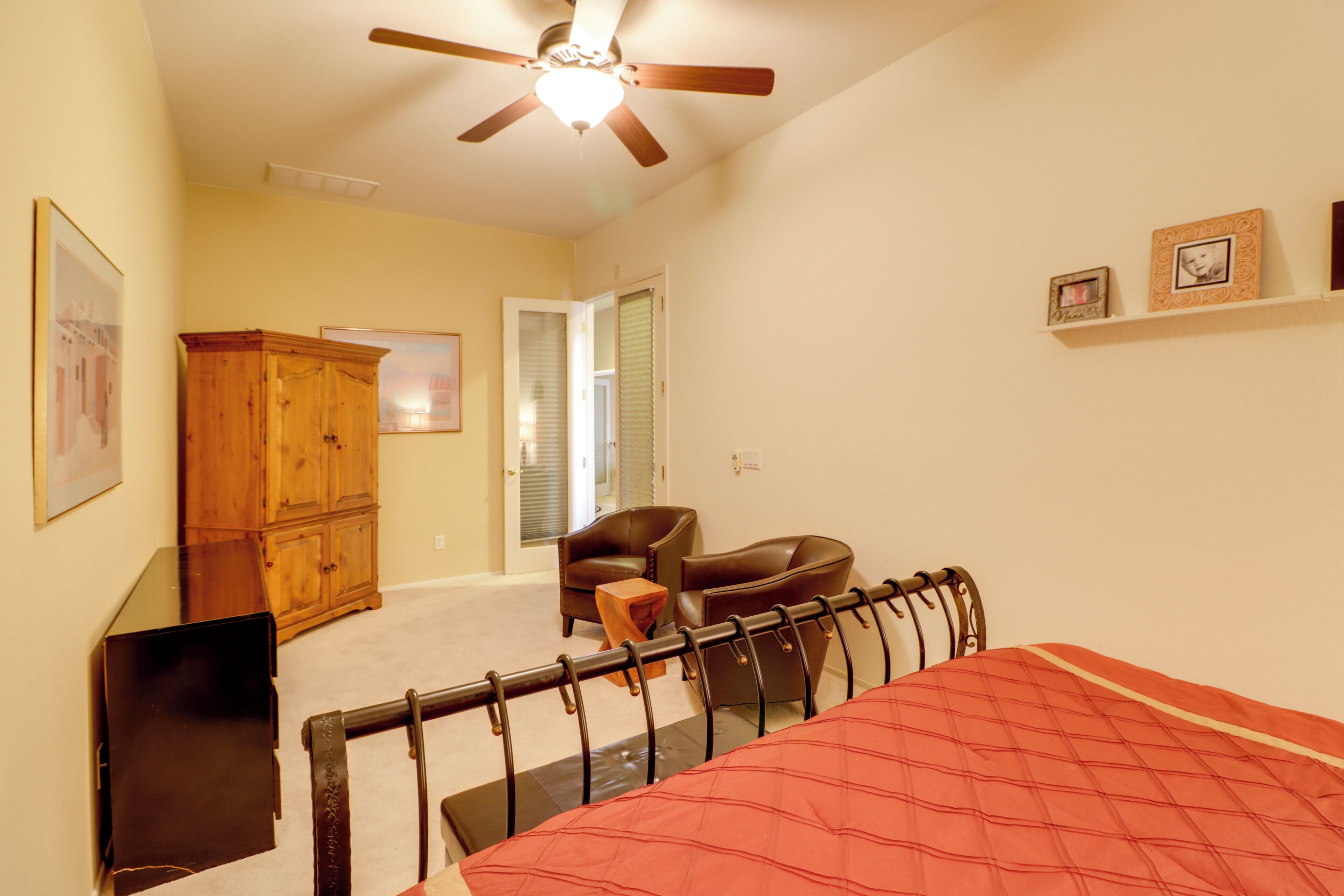 Une chambre à coucher comprenant un lit, un ventilateur de plafond, une armoire en bois, une chaise et une petite table.