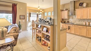 A spacious living area with a sofa, coffee table, and decorative items. A kitchen area with wooden cabinets and a countertop is visible.