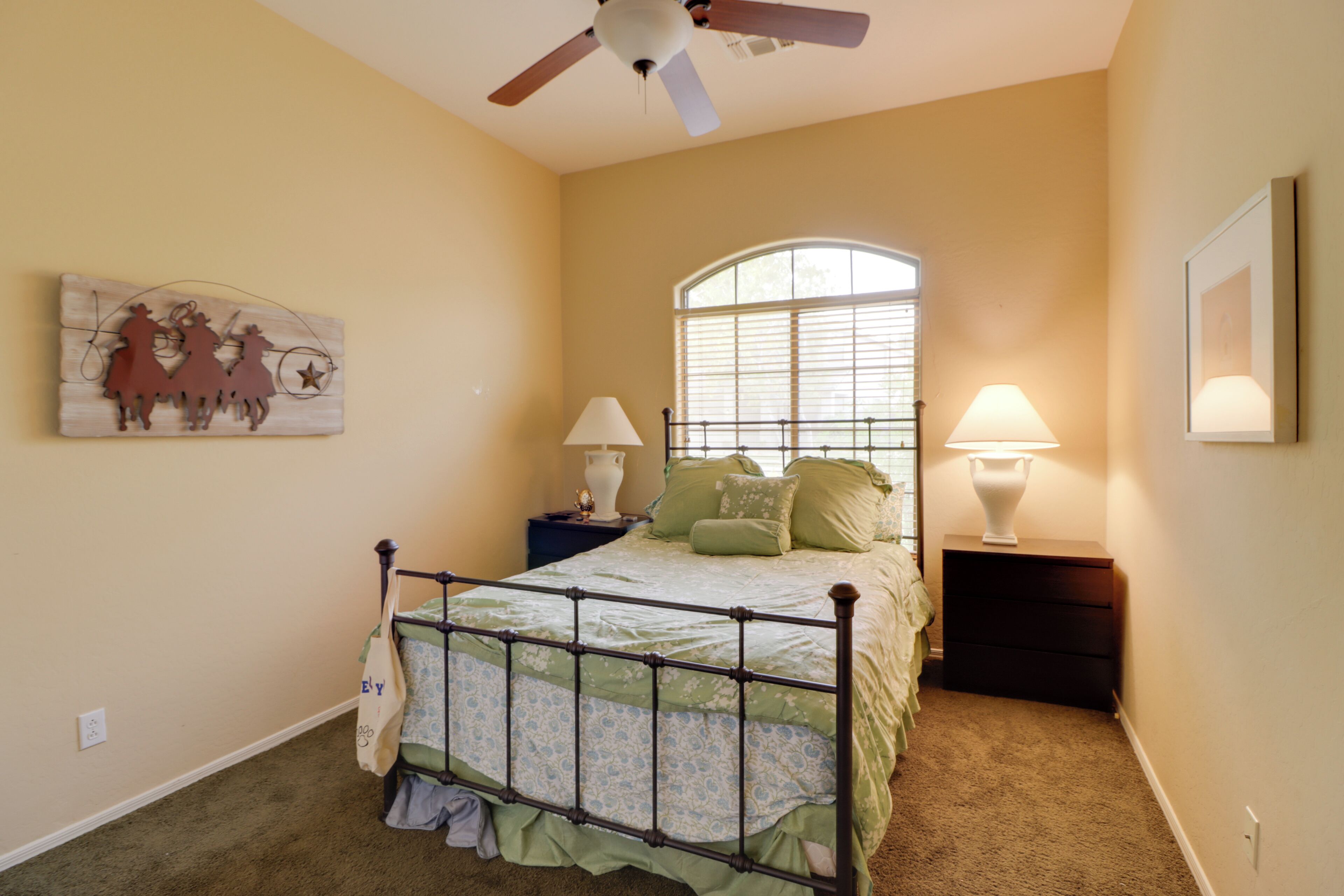 A bedroom with a bed, two nightstands, a ceiling fan, a window, and a wall decoration.