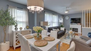 A modern living room with a dining table set for four, a sofa, a fireplace, and a television.