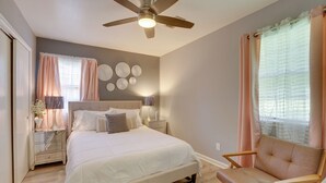 A bedroom with a bed, a chair, a nightstand, a lamp, and a ceiling fan.