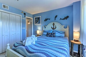 A bedroom with a bed, a wardrobe, a nightstand with a lamp, and wall decorations including fish and a painting.