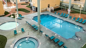 A hotel pool area with multiple pools, lounge chairs, and a covered seating area.