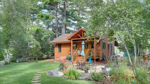 A log cabin with a porch, surrounded by a garden with stepping stones and potted plants. - Lakefront Cabin w/ Private Dock & Fire Pit! (Minocqua)