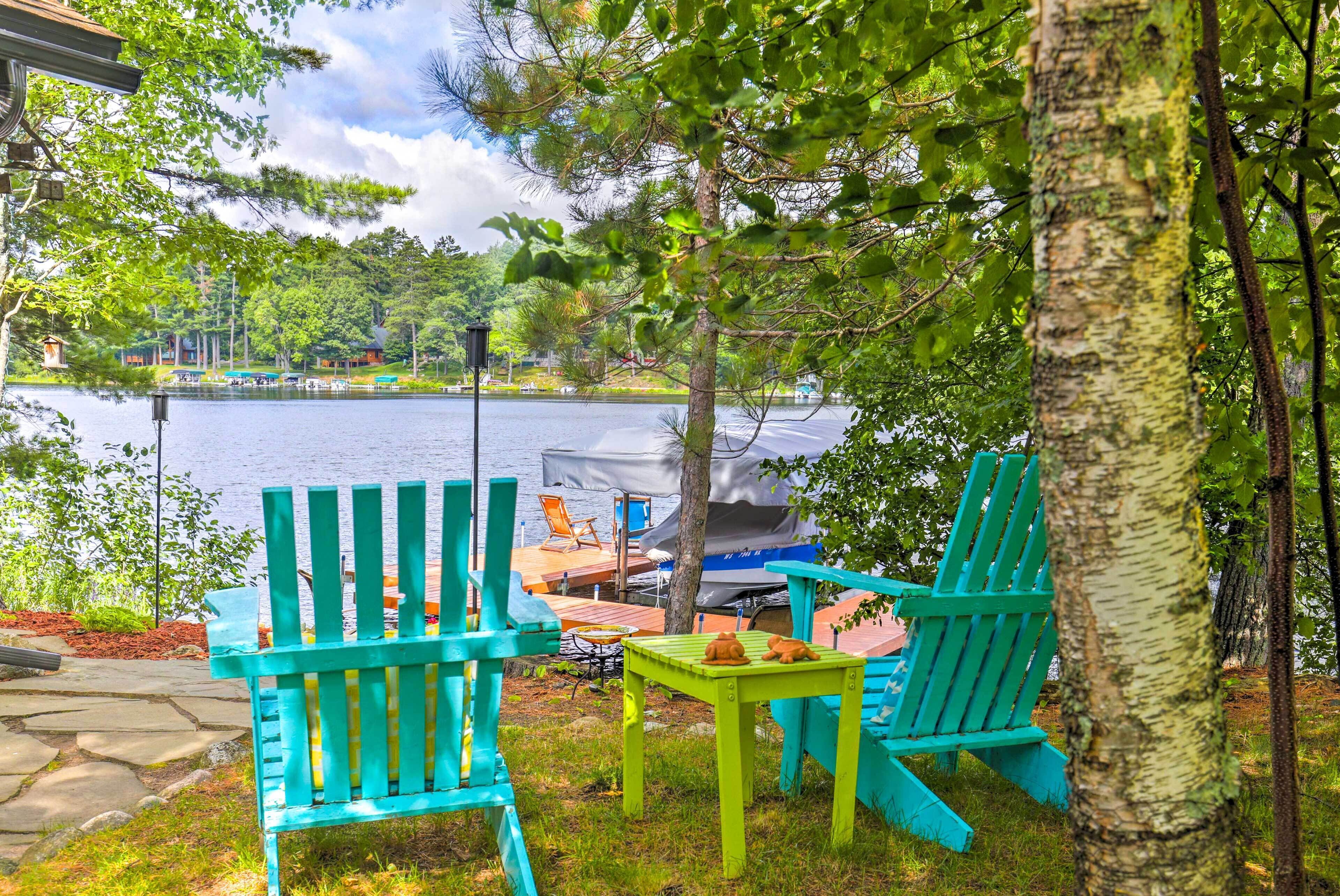 Outdoor seating with chairs and a table, a dock with a boat, and a lake view.