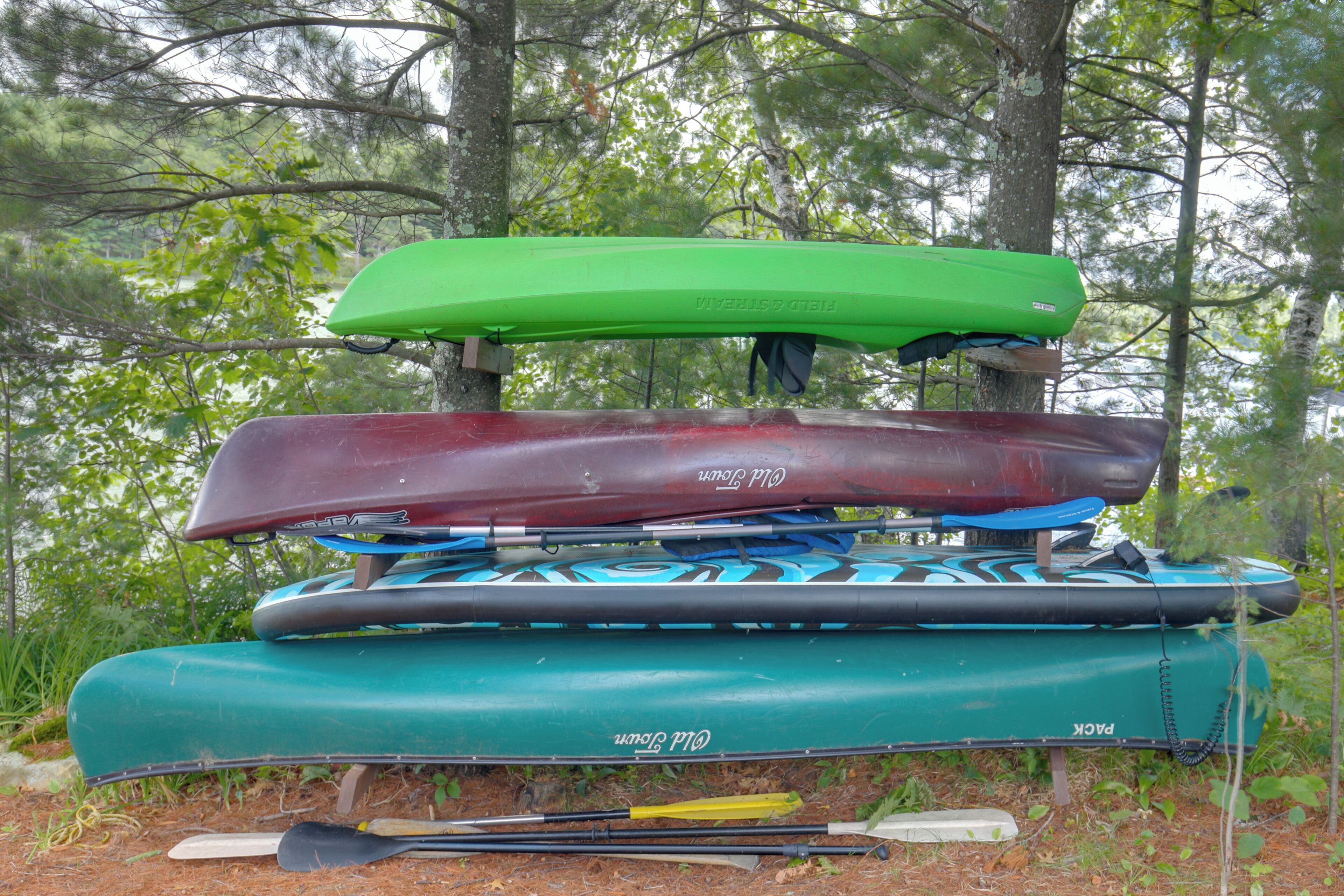 Een stapel kajaks en paddleboards in een bebost gebied.