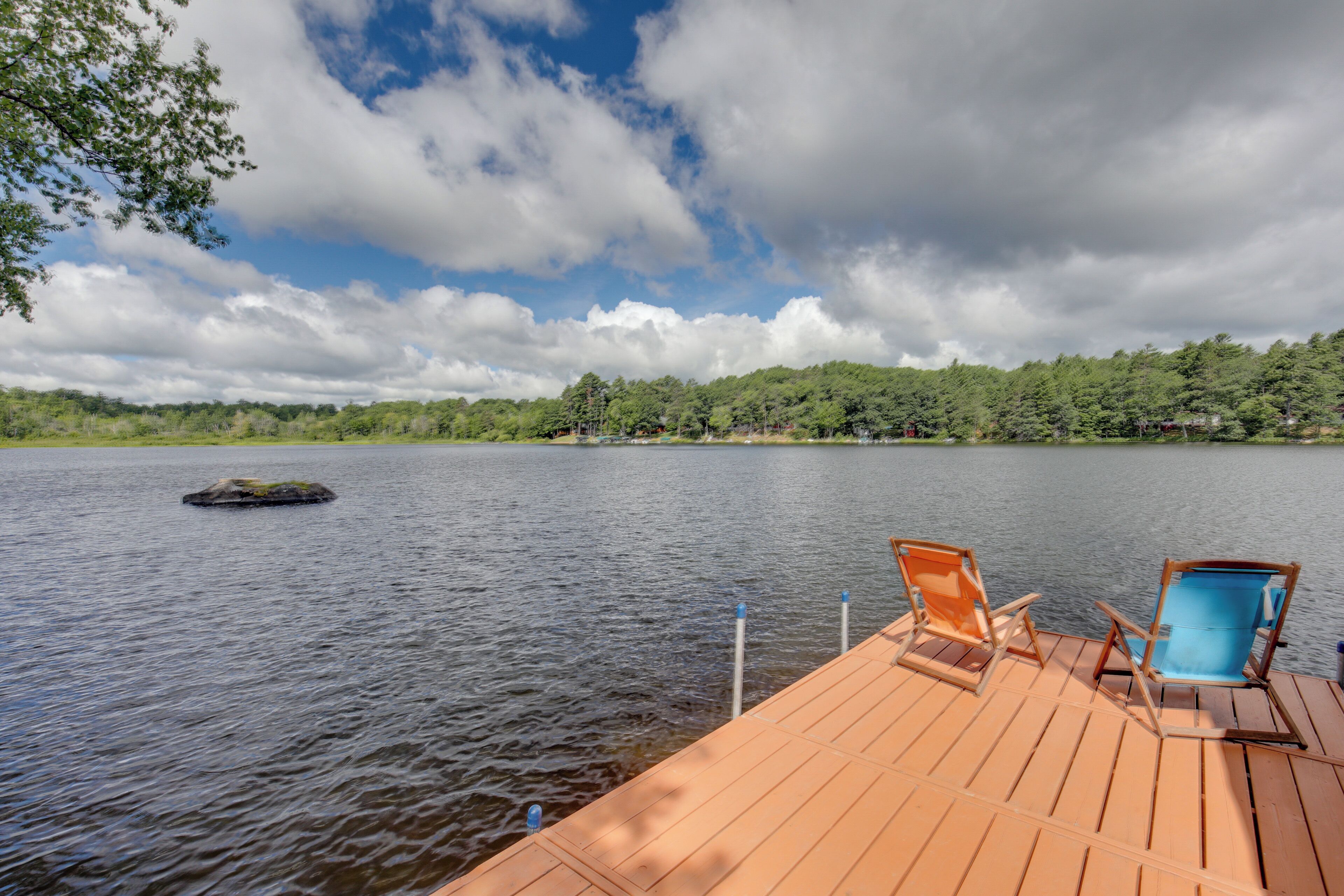 Un patio in legno con due sedie e una piscina, con vista su un lago e una riva boscosa con una piccola isola.