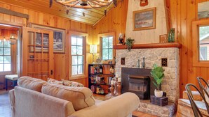 A cozy log cabin interior with a stone fireplace, wooden walls, and a large wooden ceiling fan. - Lakefront Cabin w/ Private Dock & Fire Pit! (Minocqua)