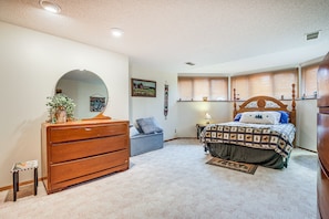 A bedroom with a wooden dresser, a bed with a patterned bedspread, a small stool, and a mirror on the wall.