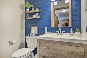 A bathroom with a blue wall, white toilet, and a vanity with a mirror and sink.