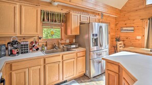 A kitchen with wooden cabinets, a stainless steel refrigerator, and a window with curtains. - Grand Windham Retreat w/ Fire Pit & Game Room (Windham)