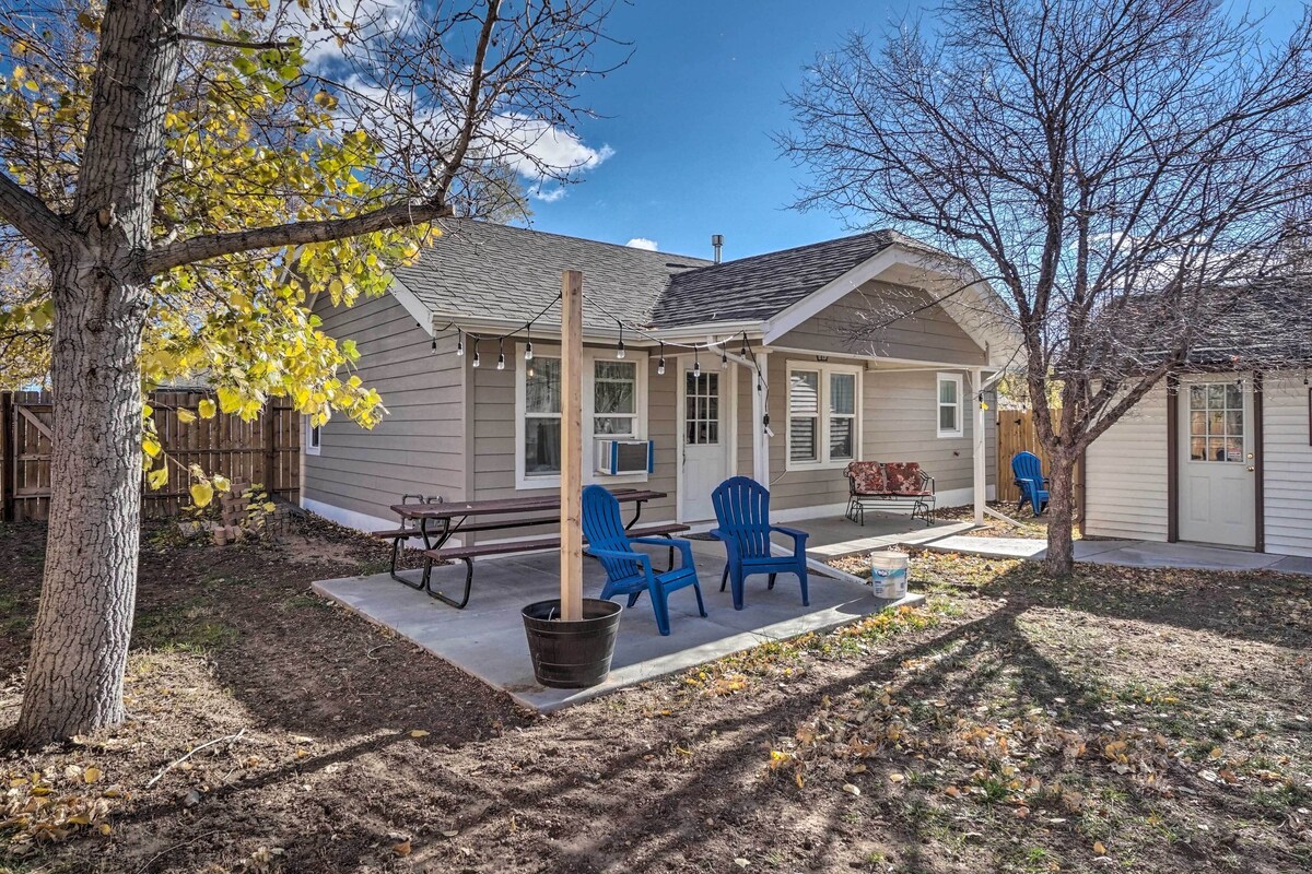 A residential house with a covered patio, two blue chairs, a picnic table, and a wooden fence.