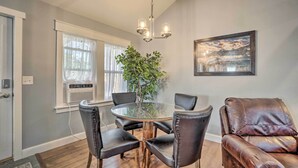 Un coin repas avec une table ronde en verre, des chaises en cuir noir, un canapé en cuir marron, une grande plante en pot et un tableau représentant un paysage, encadré et accroché au mur.