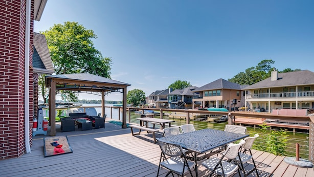 A wooden deck with outdoor furniture, a covered seating area, and a view of a body of water and buildings in the background. - Beautiful Montgomery Home w/ Lakefront Deck! (Montgomery)