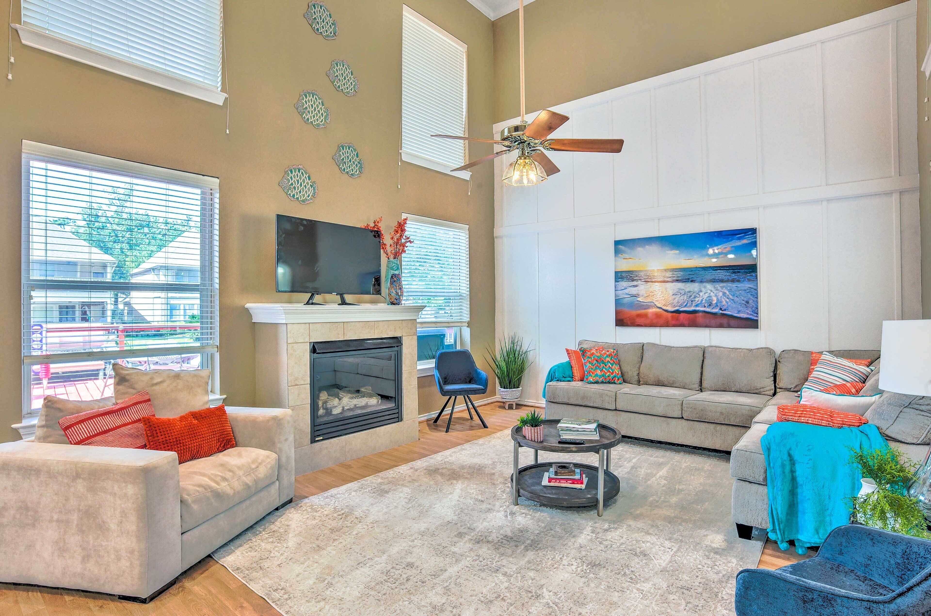 A spacious living room with a fireplace, a ceiling fan, and a large window.