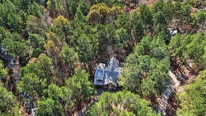 An aerial view of a cabin surrounded by dense forest.