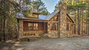 A stone cabin with a wooden deck, large windows, and a chimney.