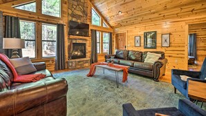 A cozy log cabin interior with a fireplace, leather sofas, and a stone accent wall.