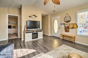 A living room with a flat-screen TV, a fireplace, a bench, and a wall with hats and a mirror. - Oak Island Hideaway Hut ~ 1 Mi to Long Beach! (Oak Island)