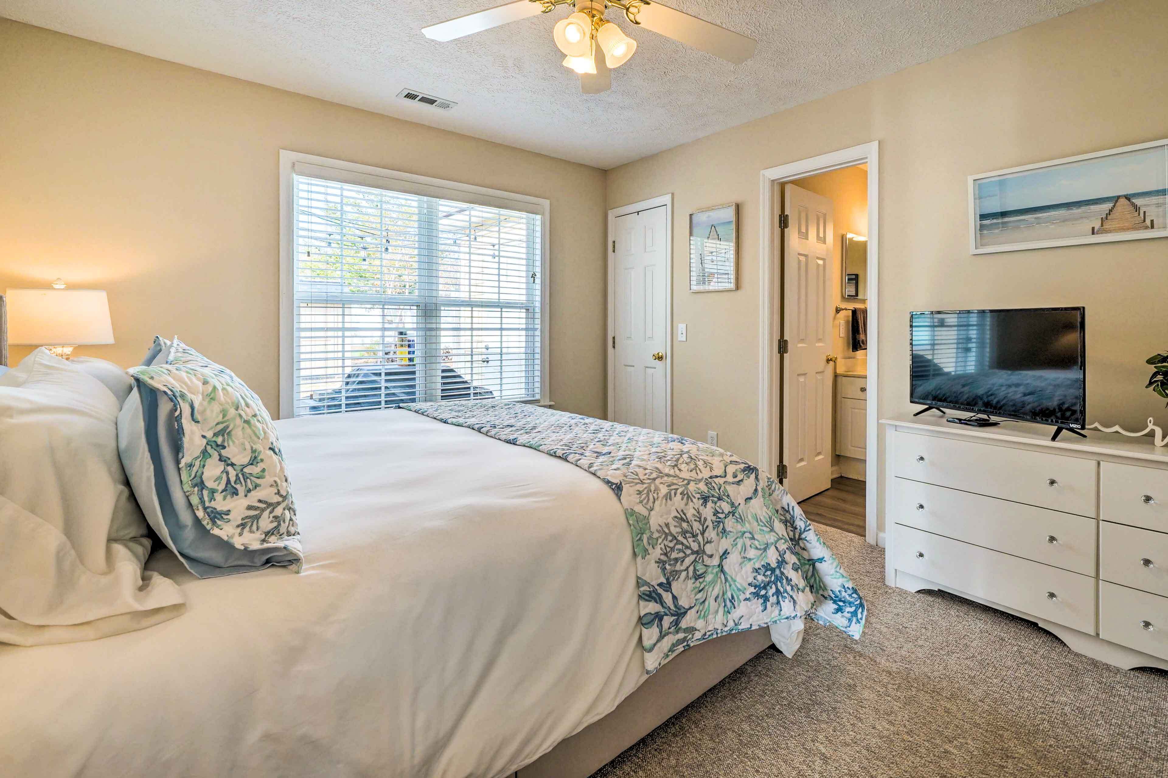 A bedroom with a bed, a TV, a dresser, and a window with blinds.