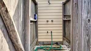 A narrow wooden pathway leading to a beige door with two outdoor faucets and a green hose. - Oak Island Hideaway Hut ~ 1 Mi to Long Beach! (Oak Island)