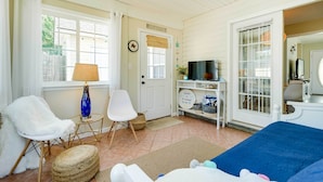 A cozy room with a bed, a chair, a lamp, a television, and a door with a welcome sign. - Oak Island Hideaway Hut ~ 1 Mi to Long Beach! (Oak Island)