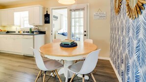A kitchen with white cabinets, a dining table with chairs, and a hanging light fixture. - Oak Island Hideaway Hut ~ 1 Mi to Long Beach! (Oak Island)
