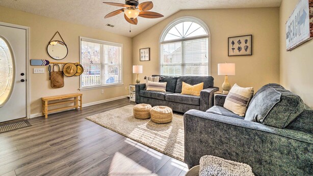A living room with a dark gray sofa, a wooden bench, and a ceiling fan. - Oak Island Hideaway Hut ~ 1 Mi to Long Beach! (Oak Island)