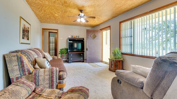 A cozy living room with a ceiling fan, a television, and a large window with blinds. - Charming Subiaco Getaway Near Arkansas River! (Subiaco)