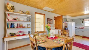 A dining area with a wooden table, chairs, and a kitchen in the background. - Charming Subiaco Getaway Near Arkansas River! (Subiaco)