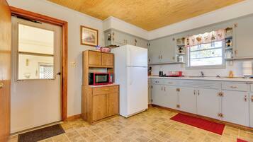 A kitchen with wooden cabinets, a white refrigerator, and a microwave on a wooden shelf.