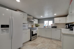 A modern kitchen with white cabinetry, a built-in oven, a microwave, and a coffee maker.