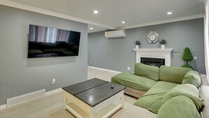 A living room with a flat-screen TV, a sofa, a coffee table, a fireplace, and recessed ceiling lights. - Deck + Yard: Pet-friendly Apartment in Magna! (Magna)