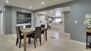 A modern kitchen with white appliances, a dining area with a wooden table and chairs, and a gray accent wall. - Deck + Yard: Pet-friendly Apartment in Magna! (Magna)