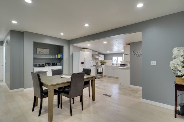 A modern kitchen with white appliances, a dining area with a wooden table and chairs, and a gray accent wall.