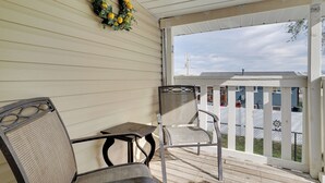 A covered porch with two chairs and a table, a wreath on the wall, and a view of a fenced yard. - Deck + Yard: Pet-friendly Apartment in Magna! (Magna)