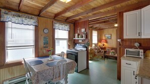 A cozy cabin interior with a dining table, chairs, a kitchen area with a stove, and a living space with a couch and lamp. - 'grandma's Cottage' w/ Sunroom: Walk to Beach (Old Saybrook)